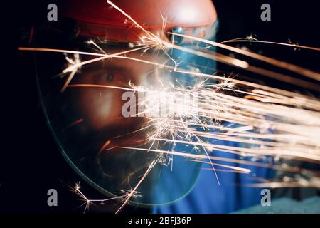 Mann Arbeiter in transparenter Schutzmaske arbeitet auf Metall mit Kreissäge Schleifer. Funken und Gesicht. Stockfoto