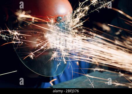 Mann Arbeiter in transparenter Schutzmaske arbeitet auf Metall mit Kreissäge Schleifer. Funken und Gesicht. Stockfoto
