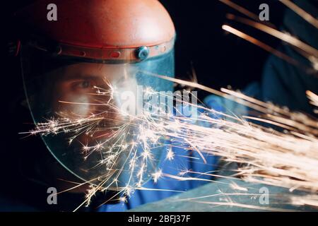 Mann Arbeiter in transparenter Schutzmaske arbeitet auf Metall mit Kreissäge Schleifer. Funken und Gesicht. Stockfoto