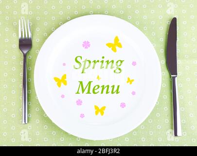 Teller mit Text 'Spring Menu', Gabel und Messer auf Tischdecke Hintergrund Stockfoto