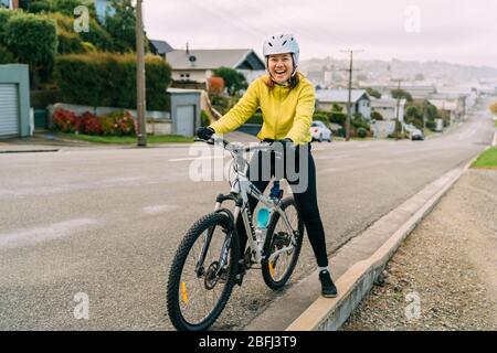 18/04/2020-Asiatische Frau macht bergauf mit Mountainbike. Eine Frau, die sehr müde war und auf der Straße in Oamaru, Neuseeland, anhält. Stockfoto