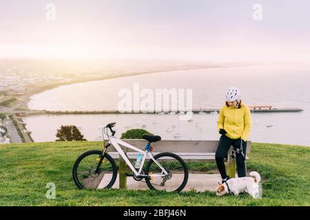 Asiatische Frau machen bergauf mit Mountainbike. Eine Frau, die ein Foto am Aussichtspunkt mit einem Hund in Oamaru, Neuseeland, macht. Stockfoto