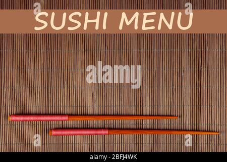 Paar Essstäbchen und Sushi-Menü Text auf braunem Bambus-Matte Hintergrund Stockfoto