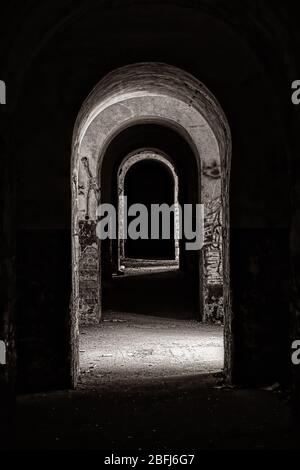 Interieur mit gewölbtem Korridor in einem verlassenen Gebäude, Licht und Schatten aus Seitenkammern, alte militärische Festung aus dem 19. Jahrhundert, urbane Explora Stockfoto