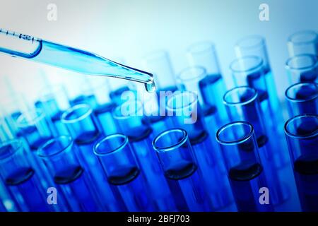 Pipette, die Flüssigkeit auf einem der Reagenzgläser auf blauem Hintergrund aufgibt Stockfoto