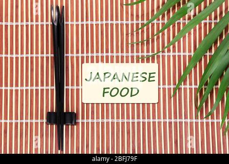 Paar Essstäbchen und japanisches Essen Text auf braunem Bambus-Matte Hintergrund Stockfoto