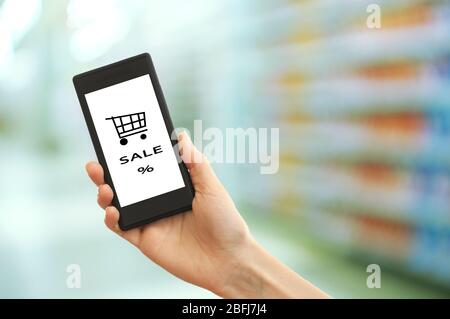 Mobile Shopping-Konzept. Hand halten Handy für Internet-Shopping auf Supermarkt Hintergrund Stockfoto