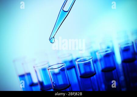 Pipette, die Flüssigkeit auf einem der Reagenzgläser auf blauem Hintergrund aufgibt Stockfoto