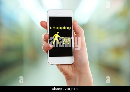 Mobile Shopping-Konzept. Hand halten Handy für Internet-Shopping auf Supermarkt Hintergrund Stockfoto