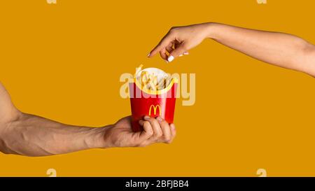 KHARKIV, UKRAINE - 4. APRIL 2020: Mann und Frau mit einer Packung pommes Frites von McDonald's auf orangefarbenem Hintergrund Stockfoto