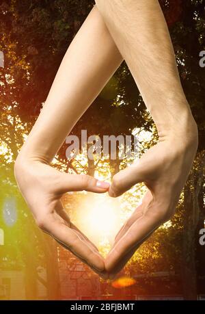 Herz von männlichen und weiblichen Händen auf Naturhintergrund geformt Stockfoto