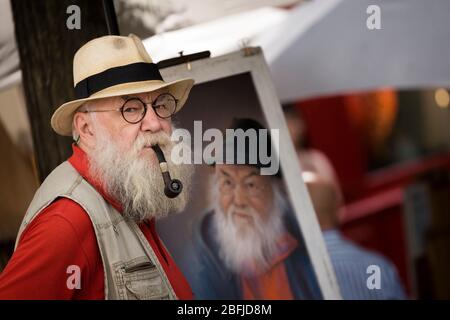 Porträt eines älteren männlichen Künstlers mit Hut, Pfeife und Bart, der vor seiner Staffelei auf dem Künstlermarkt in Montmartre, Paris, steht Stockfoto