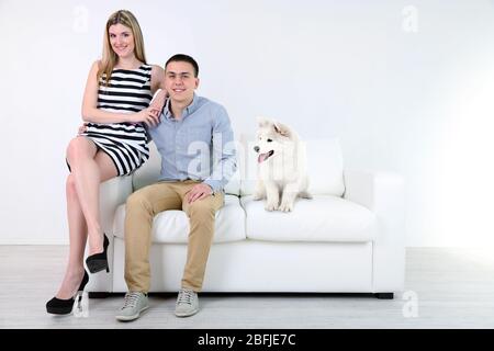 Pärchen und Hund sitzen auf Sofa, auf hellem Hintergrund Stockfoto