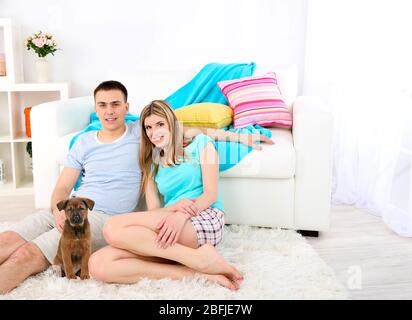 Ein Paar und ein kleiner Welpe sitzen auf einem Teppich in der Nähe des Sofas zu Hause Stockfoto