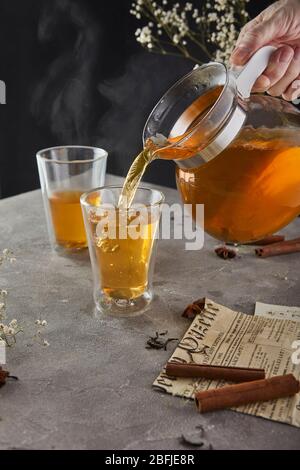 Eine Hand mit einer Teekanne gießt kochenden Tee während des Frühstücks auf grauem Hintergrund in eine Tasse. Tasse mit Dampf. Stockfoto