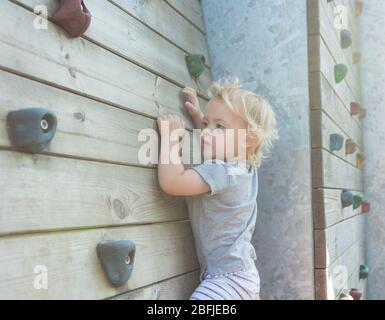 Portrait von cute blonde Mädchen klettern Kunststoff Boulderwand outdoor. Stockfoto