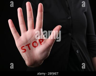 Weibliche Hand mit Wort-STOPP auf schwarzem Hintergrund Stockfoto