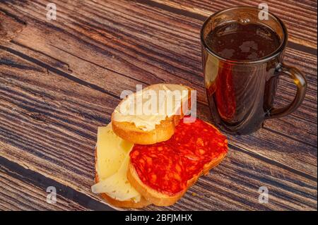 Frischer Weizentoast mit Butter und Wurst und einem Glasküken aus Tee auf Holzgrund. Nahaufnahme Stockfoto