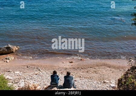 Ein Paar mit dem Rücken zur Kamera und nicht erkennbar, sitzt an einem kleinen Strand auf Mallorca. Ein Bild der Entspannung in der Natur Stockfoto