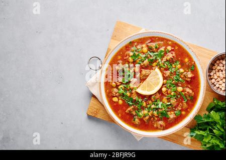 Marokkanische Harira Suppe in weißer Platte auf Holzbrett auf grauen Beton Tischplatte. Harira ist marokkanische Küche Gericht mit Lamm oder Rindfleisch, Kichererbsen, verliehen Stockfoto