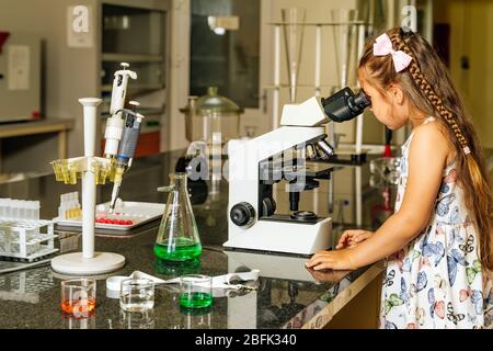 Alle Hände an Bord, kleine Helfer, eine Ärztin, die covid 19 Virusproben unter dem Mikroskop überprüft, um bei der Entdeckung der Coronavirus-Impfung zu helfen Stockfoto