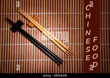 Paar Essstäbchen und chinesisches Essen Text auf braunem Bambus-Matte Hintergrund Stockfoto
