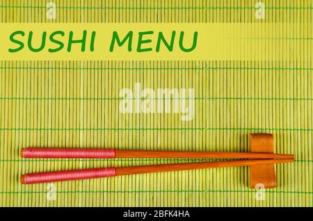 Paar Essstäbchen und Sushi-Menü Text auf grünem Bambus-Matte Hintergrund Stockfoto