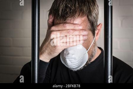 Ein Gefangener hinter Gittern trägt eine Gesichtsmaske, um Coronavirus und Covid 19 Probleme im Gefängnis zu illustrieren. Foto nach Modell gestellt. Stockfoto