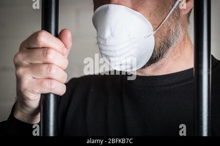 Ein Gefangener hinter Gittern trägt eine Gesichtsmaske, um Coronavirus und Covid 19 Probleme im Gefängnis zu illustrieren. Foto nach Modell gestellt. Stockfoto