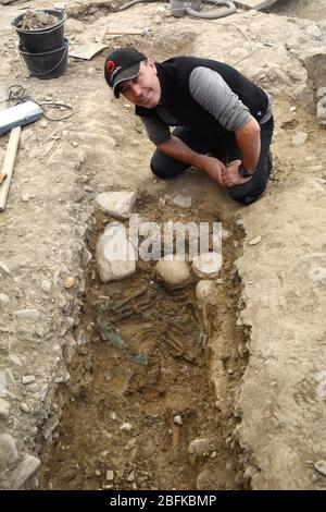 Ein Archäologe neben einem alten menschlichen Skelett, das an einer neolithischen archäologischen Stätte in der Stadt Sion im Rhonetal der Schweiz ausgegraben wurde. Stockfoto