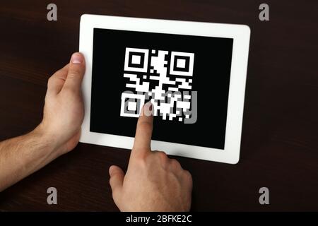 Hände, die den Tablet-PC mit QR-Code auf dem Bildschirm halten Stockfoto