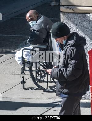 New York, USA. April 2020. Ein obdachloser Bettler mit Gesichtsmaske sieht einen Mann an, der sein Telefon in New York City benutzt. Die Regierung erklärte, dass Newyorker ihre Gesichter bedecken sollten, wenn sie nach draußen gehen und keine soziale Distanz einpflegen können, um die Ausbreitung des Coronavirus zu verhindern. Kredit: Enrique Shore/Alamy Live News Stockfoto