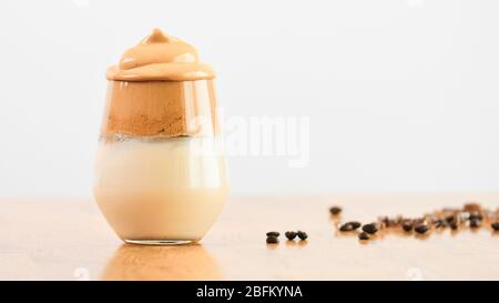 Ein Glas superschäumenden Dalgona-Kaffee auf weißem und eichenem Hintergrund mit Kaffeebohnen. Konzept für kalten Kaffee trinken und trinken, koreanische Kultur, TAS Stockfoto