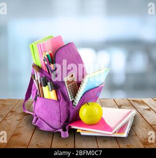 Schulrucksack auf Holztisch, auf abstraktem Hintergrund Stockfoto