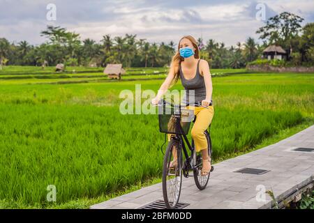 Eine junge Frau in medizinischer Maske fährt auf einem Reisfeld in Ubud, Bali, mit dem Fahrrad. Bali Travel Concept Touristen fürchten das 2019-ncov Virus. Medizinische Maskierung Stockfoto