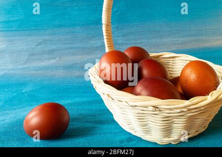 Das braune Ei liegt im hellen Korb auf dem blauen Hintergrund. Der religiöse Feiertag des osterfestes. Stockfoto