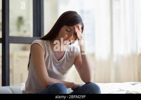 Unglückliche junge attraktive Frau, die die Stirn aus nächster Nähe hält, leidet. Stockfoto