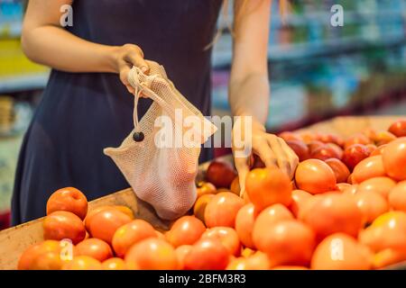 Eine Frau wählt Tomaten in einem Supermarkt ohne Plastikbeutel. Wiederverwendbare Tasche für den Kauf von Gemüse. Konzept ohne Verschwendung Stockfoto