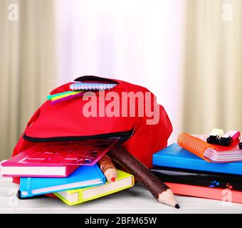 Rote Tasche mit Schulausrüstung auf Holztisch im Klassenzimmer Stockfoto