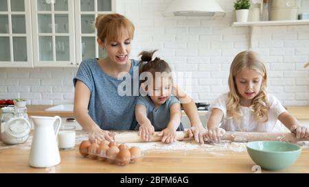 Lächelnde Mutter lehrt kleine Schwestern, Teig auszurollen. Stockfoto