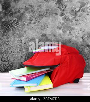 Schulrucksack auf Holztisch, auf grauem abstraktem Hintergrund Stockfoto