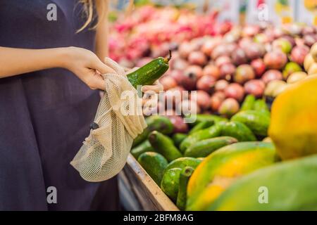 Frau wählt Avocado in einem Supermarkt ohne eine Plastiktüte. Wiederverwendbare Tasche für den Kauf von Gemüse. Konzept ohne Verschwendung Stockfoto