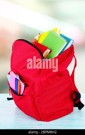 Rote Tasche mit Schulausrüstung auf Holztisch im Klassenzimmer Stockfoto