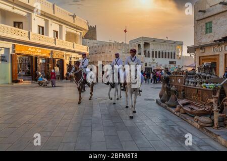 Souk Waqif Doha, Tageslichtansicht auf der Hauptstraße von Katar mit traditionellen Reitpferden der Polizei und Qatari-Flagge im Hintergrund Stockfoto