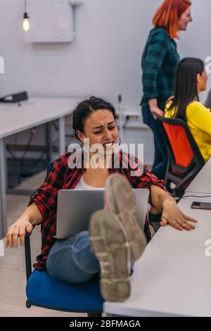 Eine nervöse Büroangestellte mit ihren Beinen auf ihrem Schreibtisch und ihrem Laptop in ihrem Schoß, die einen harten Tag hatten. Stockfoto