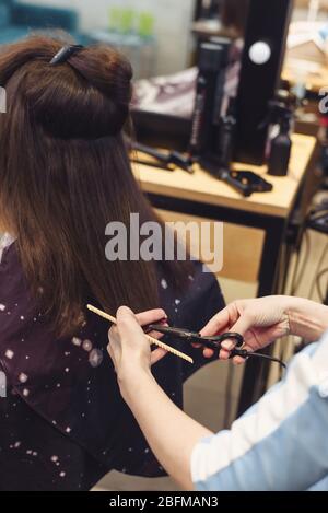Der Friseursalon schneidet die Haarspitzen einer Brunette, die in einem Schönheitssalon sitzt. Nahaufnahme des Friseursalons, der Frau mit einer Schere einen Haarschnitt zumacht Stockfoto