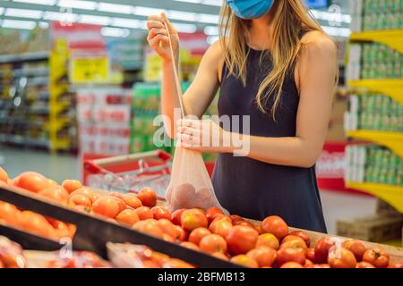 Eine Frau wählt Tomaten in einem Supermarkt ohne Plastikbeutel. Wiederverwendbare Tasche für den Kauf von Gemüse. Konzept ohne Verschwendung Stockfoto