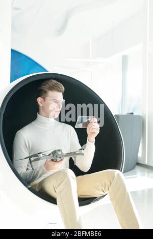 Clever junge Programmierer in smart Brillen und elegante Casualwear sitzen in semispherical Sessel während der Studie Drohne Eigenschaften Stockfoto