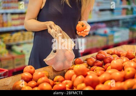 Eine Frau wählt Tomaten in einem Supermarkt ohne Plastikbeutel. Wiederverwendbare Tasche für den Kauf von Gemüse. Konzept ohne Verschwendung Stockfoto
