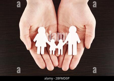 Weibliche Hände mit Familienmodell auf dunklem Holzhintergrund Stockfoto
